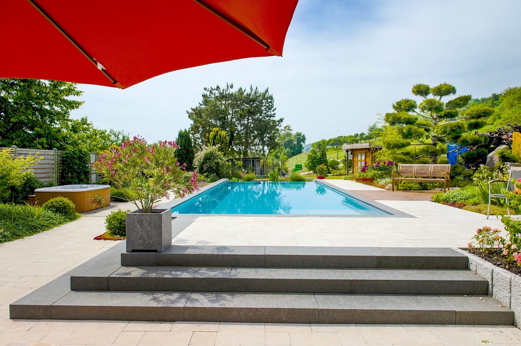 Piscine bordée de dalles claires, escalier en pierre sombre et jardin planté
