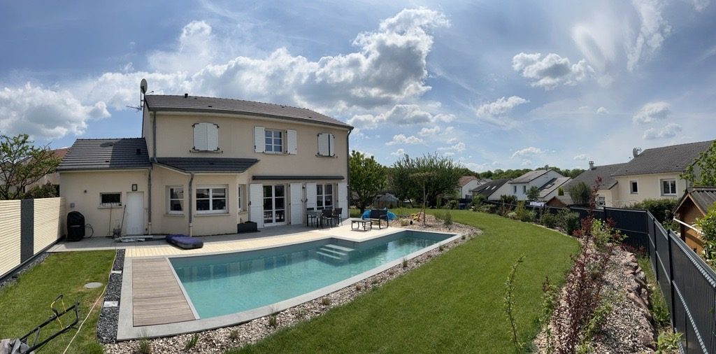 Piscine en panoramique avec plage en bois, galets et pelouse