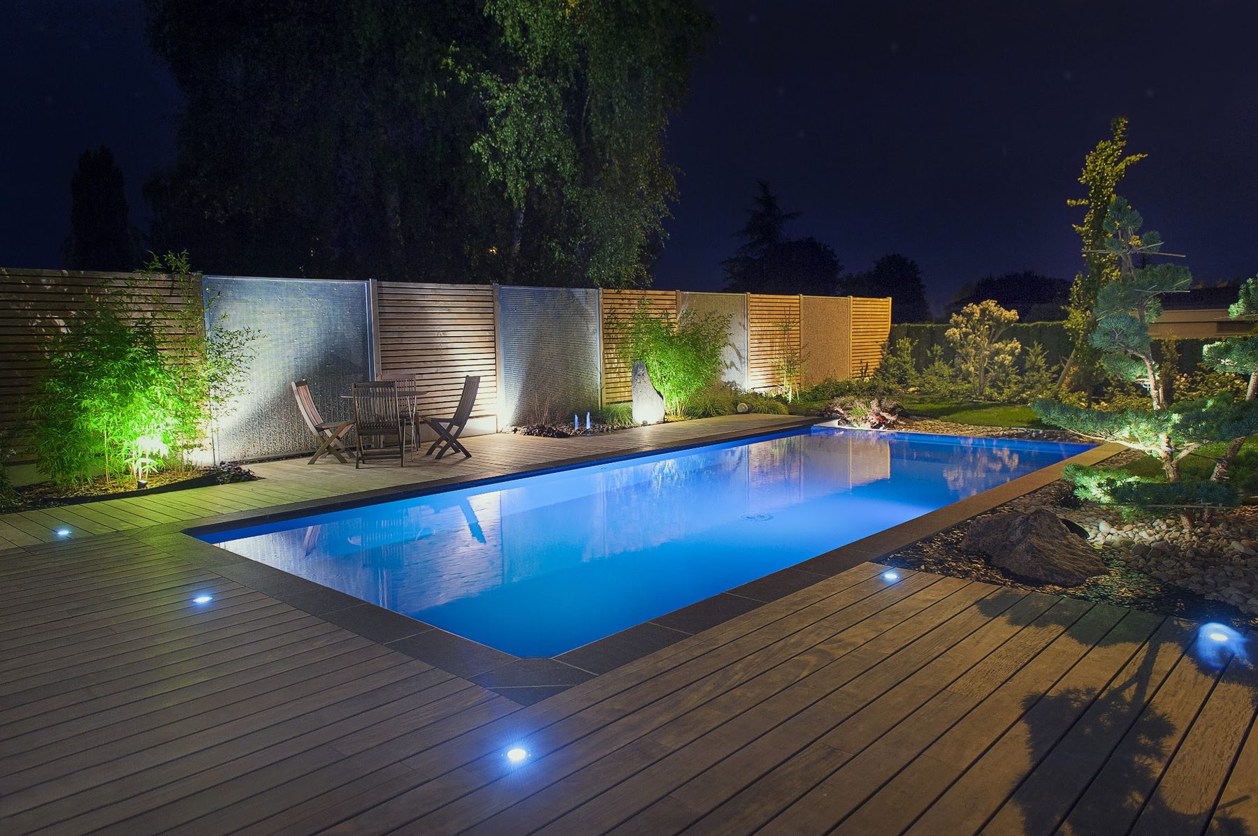Piscine éclairée la nuit, terrasse en bois, brise-vues et bambous illuminés