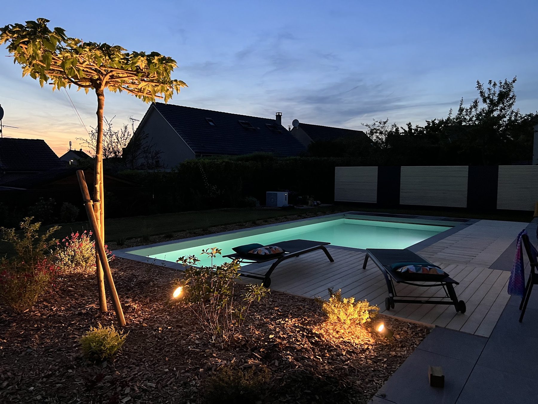 Piscine éclairée à la tombée du jour, transats et massifs illuminés